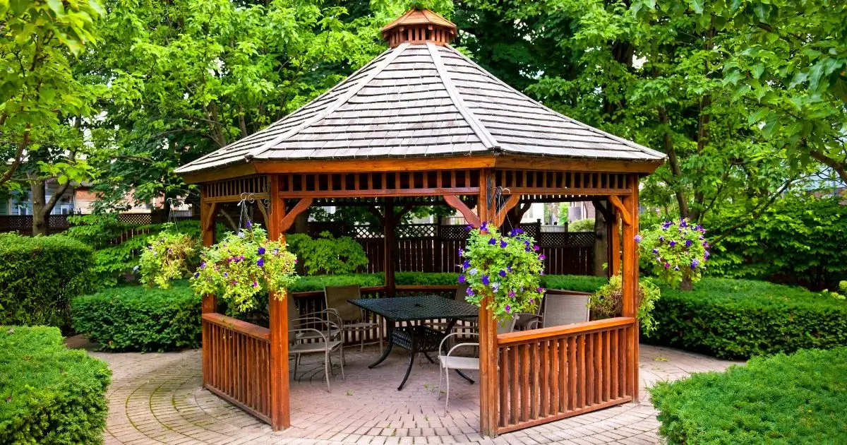 Wooden gazebo with seating surrounded by lush gardens.